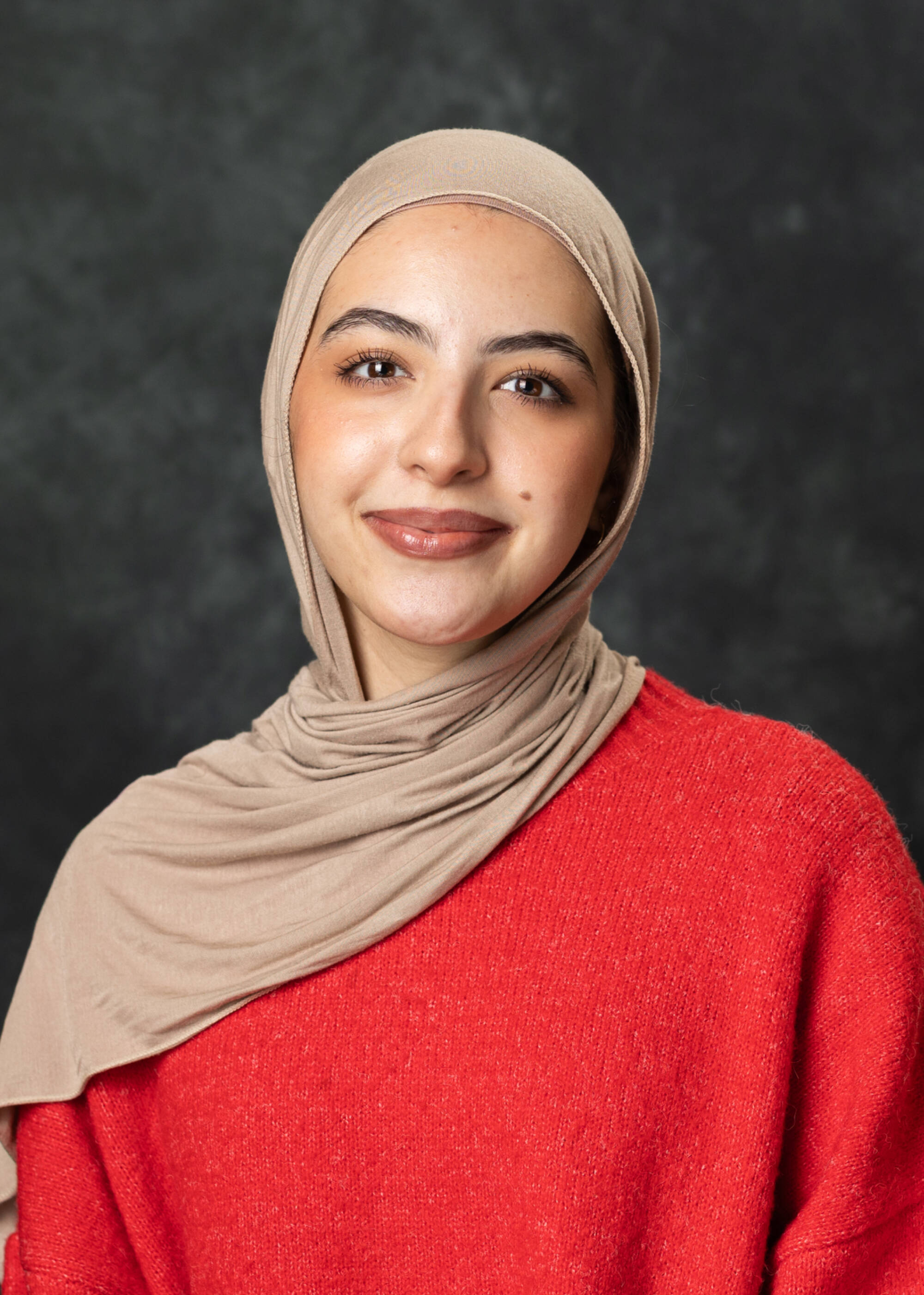 Mai Sanour smiling in a red top and tan hijab